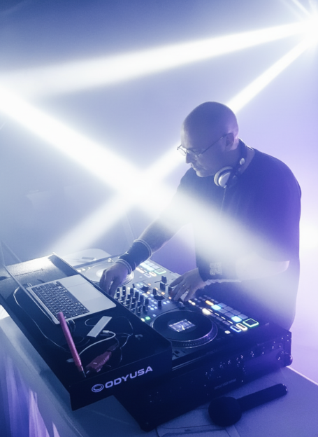 Cedric Le DJ en pleine performance derrière ses platines, sous des faisceaux lumineux blancs et violets, lors d’une soirée dansante en régio