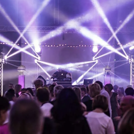 Foule en train de danser sous des faisceaux lumineux blancs et violets, avec DJ sur scène et ambiance festive lors d’un événement a lyon